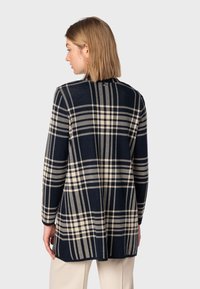 Marinblå och beige rutigt linne med långa ärmar, öppen front och avslappnad passform. Tillverkat av strukturerad tyg. Bakifrån visas designlinjer.