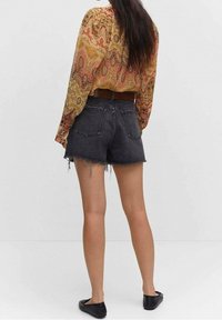 Blusa a maniche lunghe in fantasia paisley con colori caldi, abbinata a pantaloni shorts in denim nero a vita alta, con orli sfilacciati e una cintura marrone. Indossate ballerine nere.