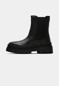 Bottine noire en cuir avec semelle crantée épaisse et panneaux latéraux élastiques, montrée de profil sur fond uni.