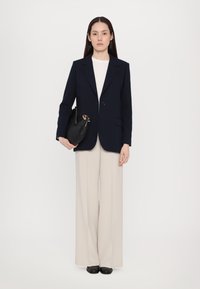 Navy blazer met één knoop, crèmekleurige top, beige wijde broek en zwarte handtas. Soepele texturen, op maat gemaakt ontwerp overal.