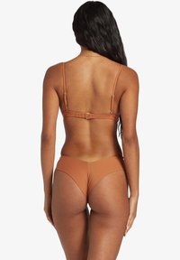 Conjunto de bikini de bronce que presenta un top de tirantes finos con cierres ajustables y braguitas de corte alto. Textura suave, diseño minimalista y color sólido.