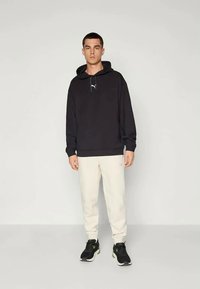 Schwarzer Kapuzenpullover mit Kordelzug und Logo, kombiniert mit hellbeigen Jogginghosen, abgerundet mit schwarzen Sneakers. Schlichte, legere Sportbekleidung.