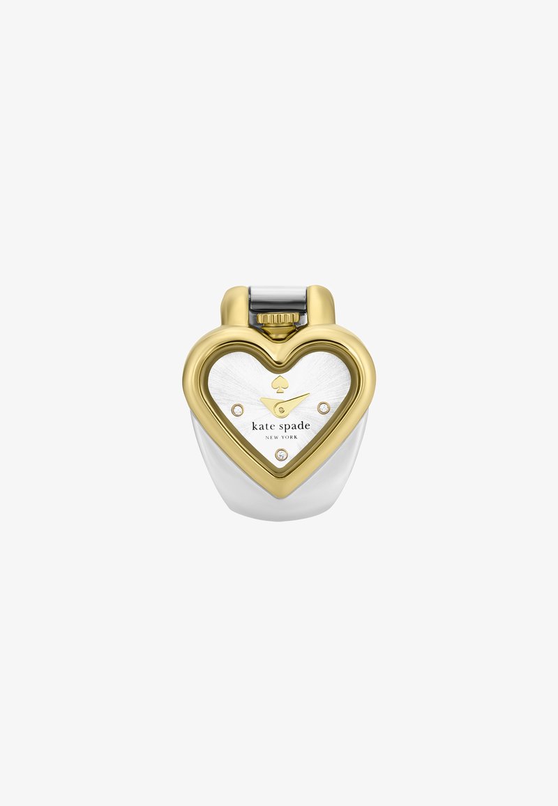 Frasco de perfume en forma de corazón con un acabado metálico dorado y blanco, que presenta un logo de trébol, un dial transparente y acentos que parecen diamantes.