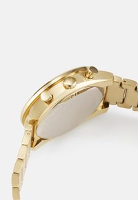 Gold-toned chronograph watch with a stainless steel strap, three pushers, and a smooth case. The back is flat and reflective.