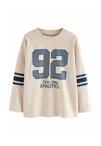 Bežinė ilgo rankovės marškinė su mėlynu "92" atspaudu, žemiau esančiu tekstu "New York Athletics" ir dviem mėlynomis horizontaliomis juostelėmis kiekvienoje rankovėje.