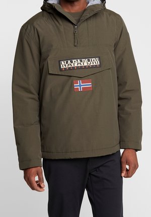 Mand iført olivengrøn Napapijri pullover jakke med halv lynlås og norsk flagpatch foran, kombineret med sorte bukser.