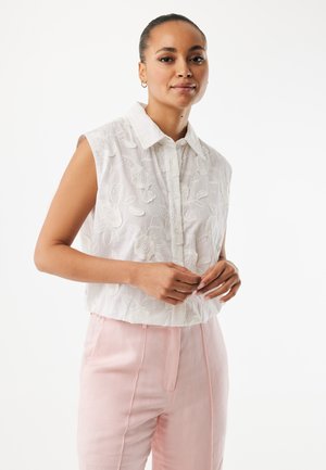 Witte mouwloze blouse met bloemrijke borduursels, kraag en knoopsluiting aan de voorkant. Gecombineerd met lichtroze, getailleerde broek.