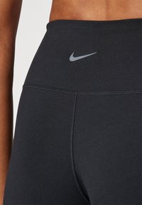 Leggings deportivos negros con una cintura alta, que presentan un sutil logo gris de Nike y costuras planas para un acabado suave.