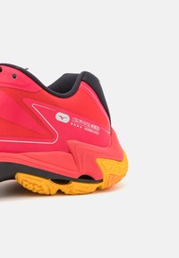 Scarpa sportiva rosa con interno nero e suola gialla. Presenta una tomaia testurizzata, un design elegante e dettagli bianchi nel branding.