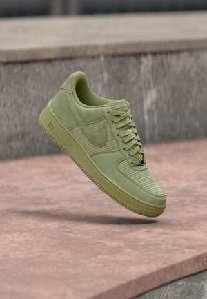 Lysegrøn Nike Air Force 1 sneaker med mesh- og ruskindsteksturer, svævende over en lyserød betonoverflade.