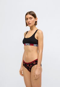 Černá braletka s červeným páskem "DIESEL", doplněná černými kalhotkami s červeným a oranžovým vzorem opic. Hladká textura, elastická látka.