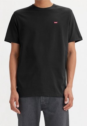 Mand iført en ensfarvet sort Levi's t-shirt og mørkegrå jeans mod en hvid baggrund.