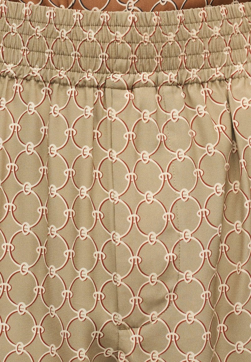 Beiger Stoff mit einem sich wiederholenden geometrischen Kettenglied-Muster in Creme und Rost, mit elastischem Raffungseinsatz am oberen Rand.