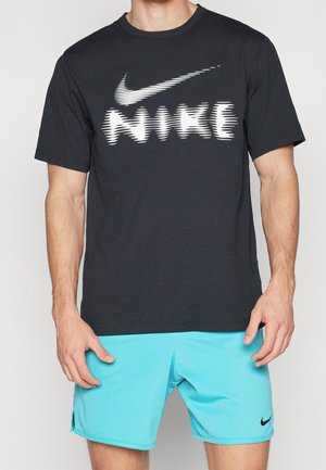Mand iført en sort Nike t-shirt med forvrænget hvidt logo og lyseblå Nike shorts med lille sort Swoosh-logo.