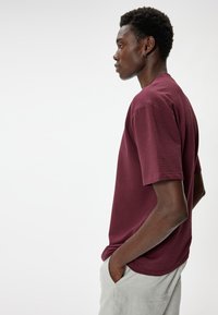 Bordeaux kortarmige textuur T-shirt met een ronde hals, gedragen met lichtgrijze broek, met een relaxte pasvorm en subtiele stiksels.