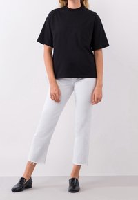 Svart kortärmad t-shirt i bomull med rund halsringning och bröstficka, matchad med vita jeans och svarta loafers.