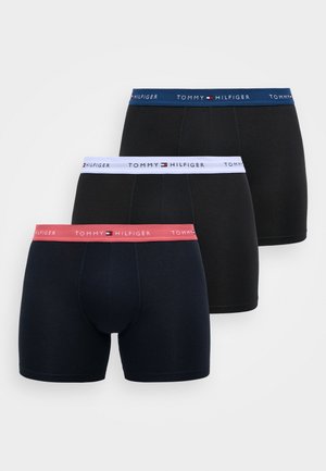 Three pairs of Tommy Hilfiger boxer shorts: black, navy, and dark navy, each with distinctive logo bands in contrasting colors. Cotton material.