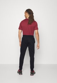 Bordová tričko s krátkym rukávom a čierne teplákové nohavice s elastickým pásom. Teplákové nohavice majú bočnú kapsu, v kombinácii so šedými a červenými športovými topánkami.