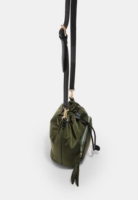 Grön nylon dragsko-väska med ett svart läderhandtag, dragkedjedetalj och en liten sidobow-accent. Har gold hardware.