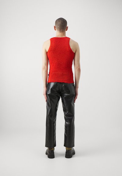 Rød smokkert tanktop med rund hals, sammen med svarte skinnbukser med rett snitt og lite glans.