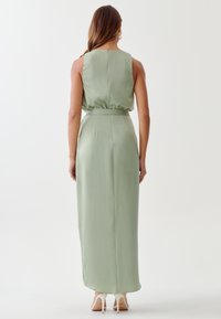 Dolga, brezrokavna, svetlo zelena satenasta obleka s prilegajočim pasom in tekočim krilom. Ima gladko teksturo in dolžino do kolen.