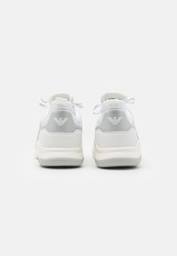 Białe sportowe sneakersy z teksturowanym szarym akcentem, posiadające wyściełany kołnierz, płaskie sznurowadła oraz logo na pięcie i z tyłu.