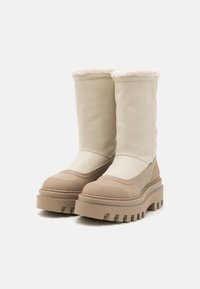Beige Kunstlederstiefel mit dicker Plattformsohle, weicher beiger Innenauskleidung und strukturiertem Gummiaußensohle. Mittlere Schafthöhe mit glatter Oberfläche.