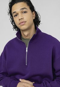 Sweat-shirt violet à fermeture éclair avec un col montant, fabriqué dans un tissu doux, doté d'une fermeture éclair argentée et de manches longues.