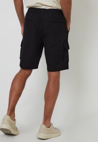 Pantalones cortos de carga negros con cintura elástica, con bolsillos frontales y traseros y un tejido texturado. Combinados con zapatillas beige.