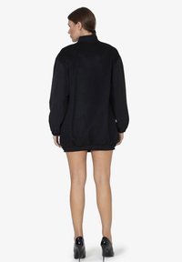 Zwarte oversized jas van een zachte, gestructureerde stof, met elastische tailleband en lange mouwen, voorzien van een hoge kraag. Weergave van de achterkant.