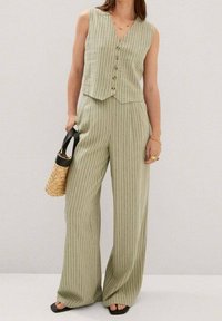Jasnozielony dwuczęściowy zestaw w paski, składający się z bezrękawnika z guzikami i spodni w szerokie nogawki. Uzupełniony plecioną torbą i czarnymi sandałami.