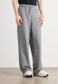 Gray sweatpants with an elastic waistband and adjustable drawstring, featuring a loose fit and soft texture, paired with white sneakers.