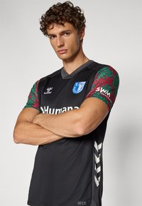 Black sports jersey featuring short sleeves with a patterned red and green design. Displays logo and text "1.FC Magdeburg."