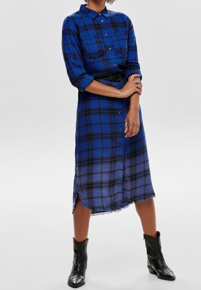 Niebieska sukienka koszulowa w kratę z zapięciem na guziki z przodu, kołnierzykiem, podwiniętymi rękawami i postrzępionym dołem. Zestawiona z czarnymi botkami za kostkę.