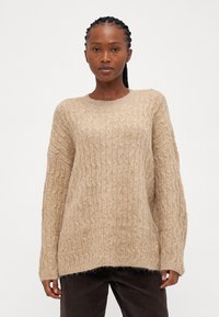 Beige kötött pulóver, textúrált sodrott mintával, kerek nyakkivágással és hosszú ujjakkal, enyhén rojtos szegéllyel.