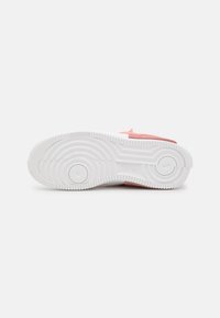 White sneaker outsole with textured grip patterns, featuring a pink accent at the heel. Rounded design with a pronounced circular motif.