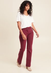 Bordeauxkleurige broek met een aansluitende taille en wijde benen, voorzien van twee decoratieve knoopaccenten. Gecombineerd met een effen witte V-hals t-shirt.