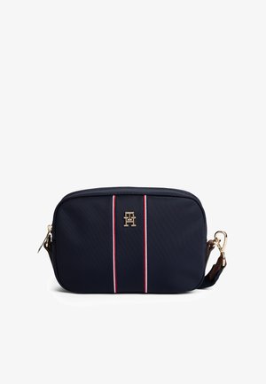 Marineblauwe rechthoekige crossbodytas met rode en witte verticale strepen en gouden logo in het midden, voorzien van een afneembare riem met gouden gesp.