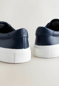 Navy bőr sportcipők sima felülettel, fehér gumitalppal és dombornyomott logóval a saroknál. Lekerekített forma, minimalista stílus.