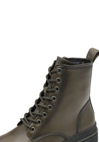 Tmavě olivově zelená kožená vojenská bota s černou gumovou podrážkou, kovovými očky, kulatými šňůrkami s vzorem a značkovým poutkem na zadní straně.