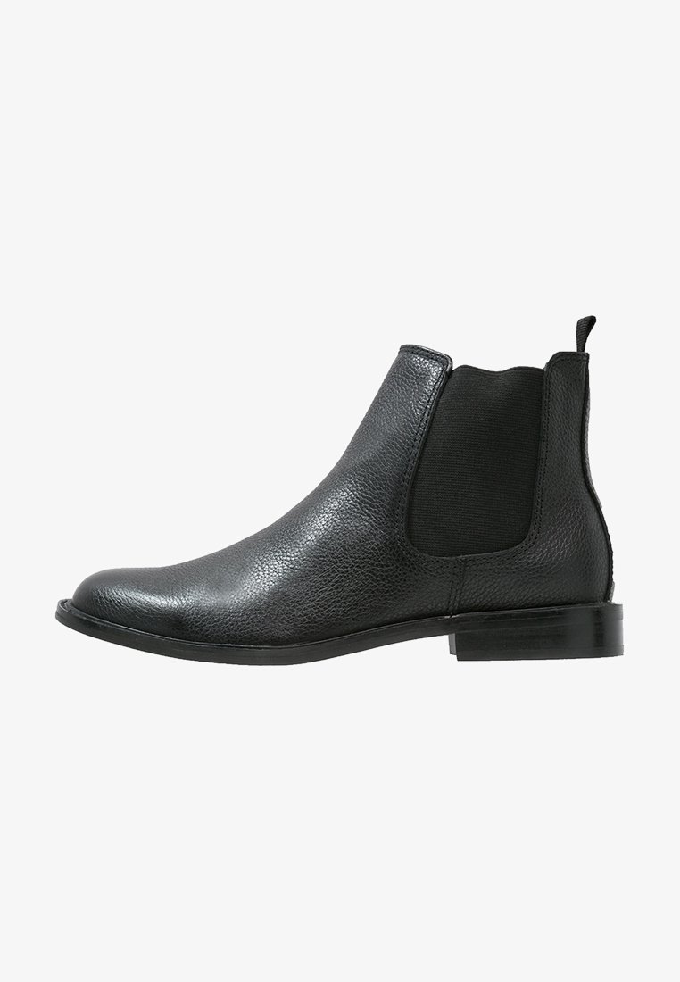 Bottine Chelsea en cuir noir avec panneau latéral élastique, languette de traction au talon et petit talon sur fond blanc.