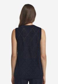 Marinblå ärmlös stickad topp med ett mönster av öppet arbete i diamantform, ribbad halsringning och fåll, samt strukturerad tyg.