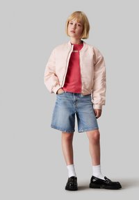 Chaqueta bomber rosa claro, camiseta roja acanalada, pantalones cortos de mezclilla, calcetines blancos, zapatos negros. Material suave, corte relajado, estilo casual.
