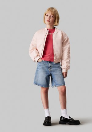 Veste bomber rose clair, t-shirt rouge à cotes, shorts en denim, chaussettes blanches, chaussures noires. Matériau doux, coupe décontractée, style casual.