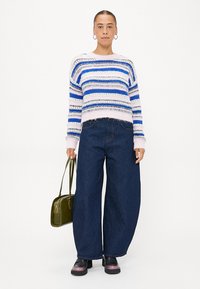 Strikkegenser med blå og hvite striper, kombinert med vide mørk denimbukser. Tilbehøret inkluderer en grønn veske og kraftige svarte sko.