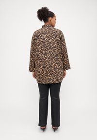 Manteau oversize en imprimé léopard avec des manches longues, en tissu doux, associé à un pantalon noir à taille cintrée et des escarpins. Texture lisse, coupe décontractée.