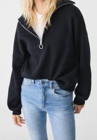 Sudadera negra de pulóver con media cremallera, cuello y puños acanalados, combinada con unos vaqueros de mezclilla azul claros con un ajuste clásico.