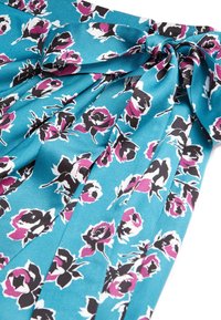 Blommönstrad tyg med turkos bakgrund, svarta och vita blommor med rosa accenter, slät textur och veckad design.