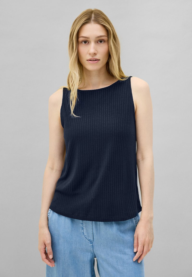 Marineblaues ärmelloses Oberteil mit gerippter Textur, Rundhalsausschnitt und lockerer Passform. Kombiniert mit hellblauen Denimhosen.