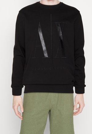 Schwarzer Langarm-Sweatshirt mit erhabenem "A|X" und "Armani Exchange" Logo, getragen von einer Person mit grüner Hose.